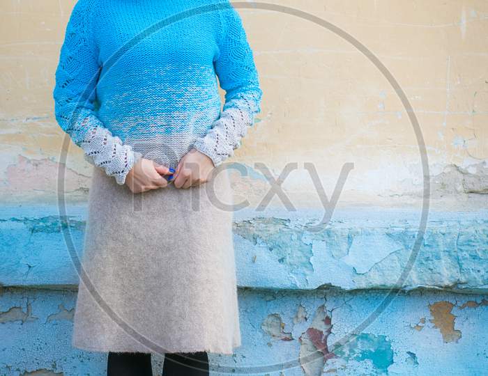 A Beautiful Young Woman With Red Hair In A Blue Sweater Made Of Natural Wool And Woolen Beige Skirt Smiling And  Posing On A City Street