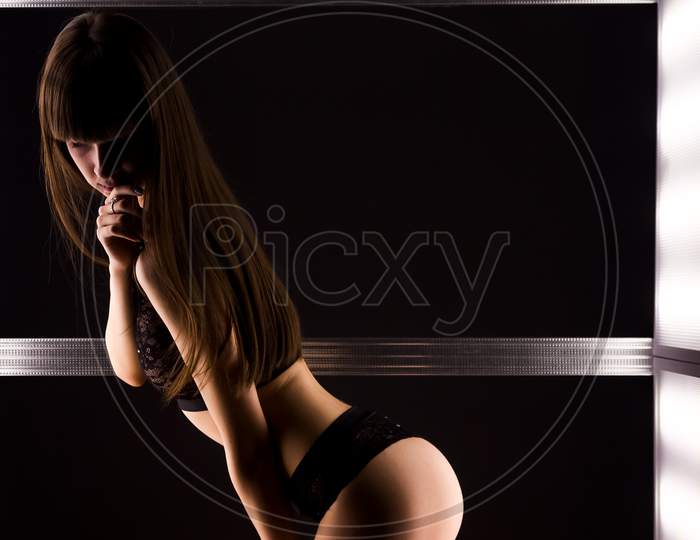Young Dark-Haired Woman In Black Lace Lingerie Posing Among Bright Lamps In A Dark Room
