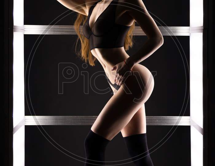 Young Dark-Haired Woman In Black  Lingerie Posing Against White Lights In Black Studio