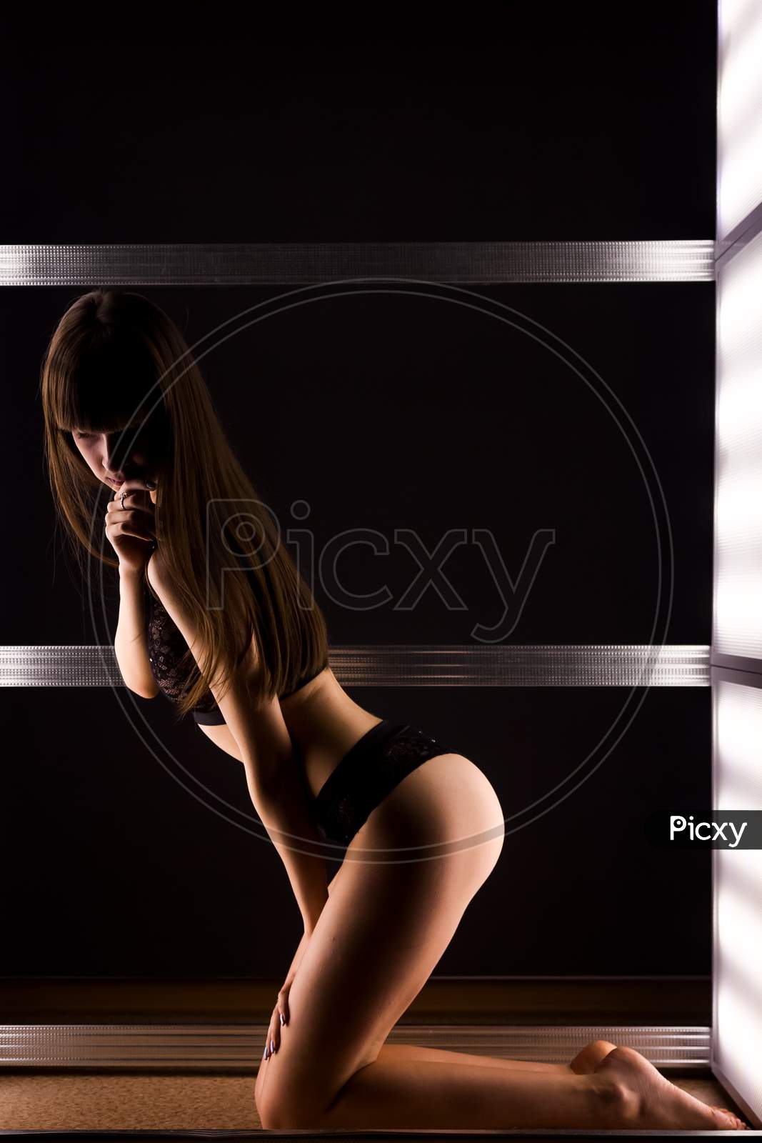 Young Dark-Haired Woman In Black Lace Lingerie Posing Among Bright Lamps In A Dark Room