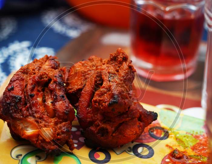 Close Up Image Of A Piece Of Fried And Roasted Chicken Tandoori Breast Piece.Its A Spicy North Indian Starter Dish. Served With Red Cranberry Juice In Glass