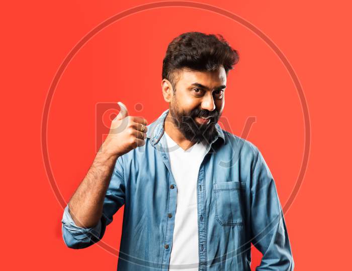 Portrait Of A Satisfied Young Indian Man Celebrating Success Isolated Over Red Background