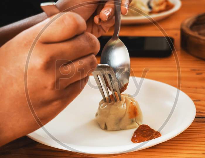 person holding eating dumpling with fork and spoon