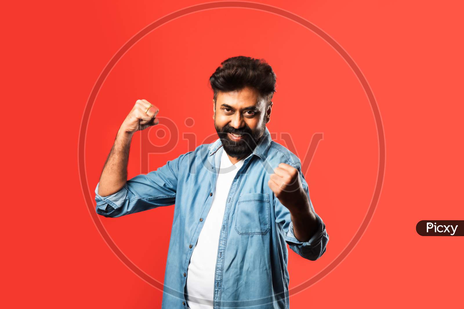 Portrait Of A Satisfied Young Indian Man Celebrating Success Isolated Over Red Background
