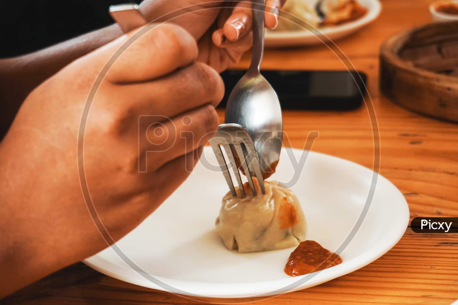 person holding eating dumpling with fork and spoon