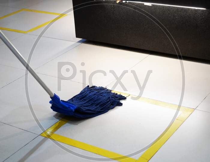 Wiping A Floor With Yellow Stripes, Using A Blue Mop