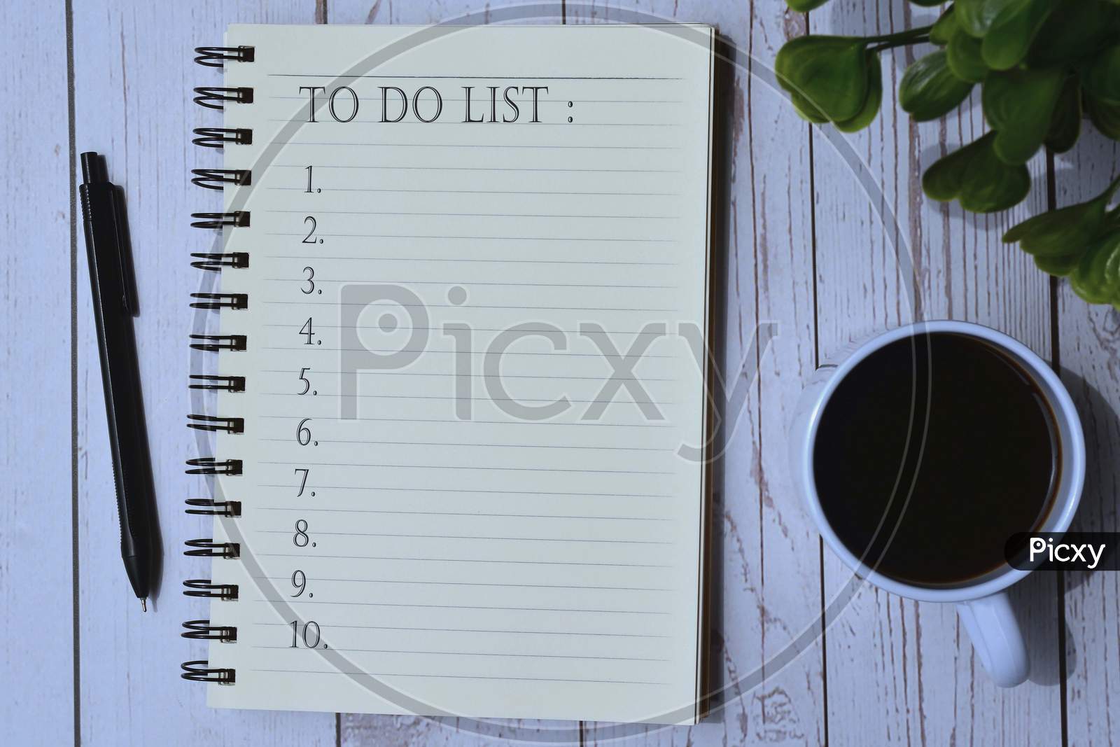 To do list on notepad with cup of coffee, pen and green leaf background on wooden desk. To do list
