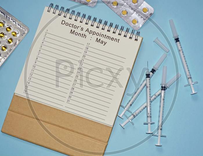 Month of May Doctor's Appointment calendar with disposable injection syringe and medicine on blue background