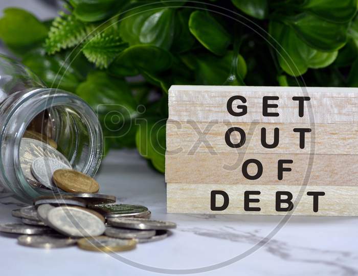 Text on wood block with blurred European coins on table surface with green plant background - Get out of debt