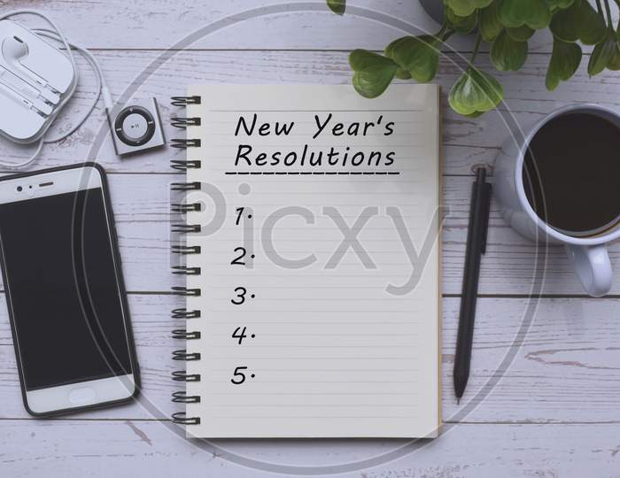 Text on notepad with cup of coffee, smart phone, music player and pen on wooden desk. New year's resolution's concept