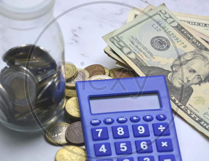 Glass jar with multicurrency coins, US dollar bills and calculator white table. Saving and travelling concept