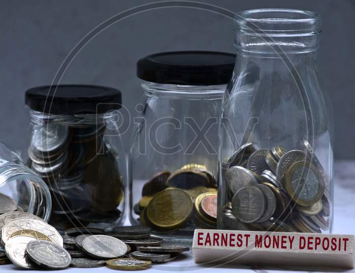 Text on wood block and glass jars with multicurrency coins - Earnest money deposit