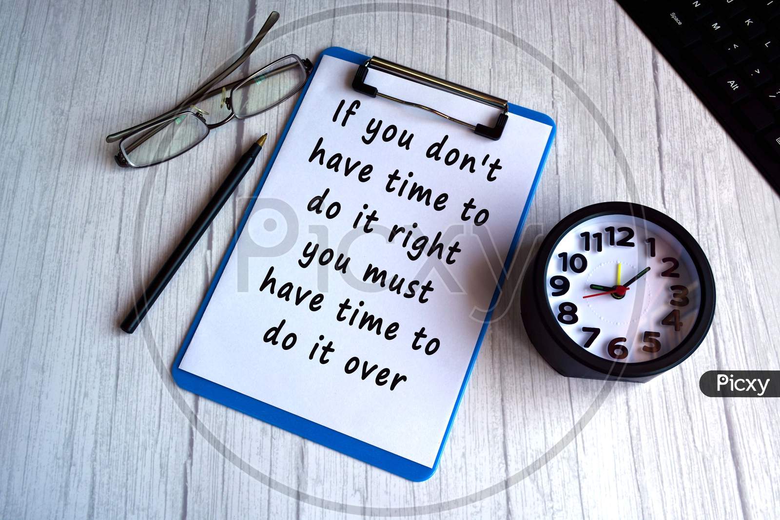 Motivational and inspirational quote on blue clip board with alarm clock, glasses, pen and keyboard on wooden desk - If you do not have time to do it right you must have time to do it over