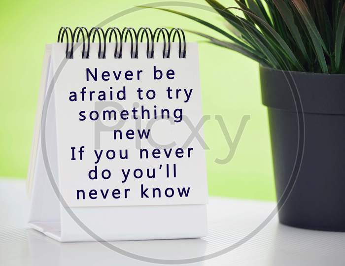 Inspirational quote on white paper stand with potted plant and blurred background - Never be afraid to try something new, if you never do you will never know