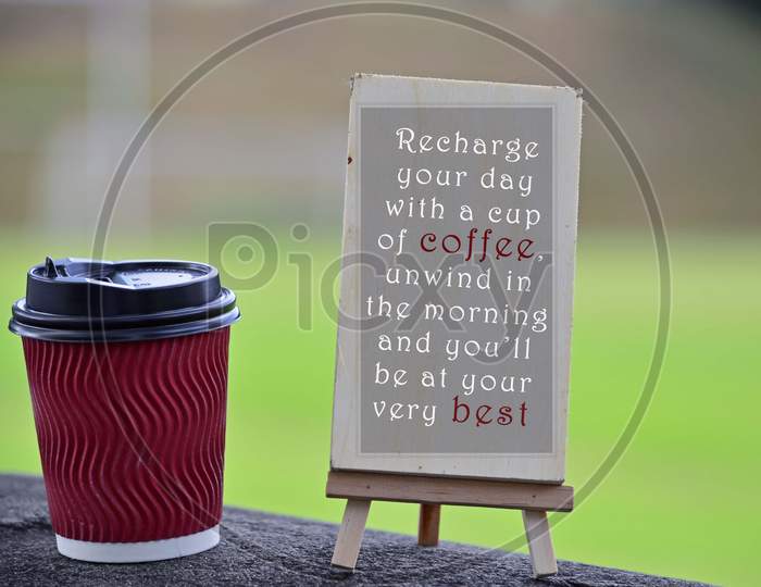 Red paper cup of coffee with text written on chalkboard and greenery background