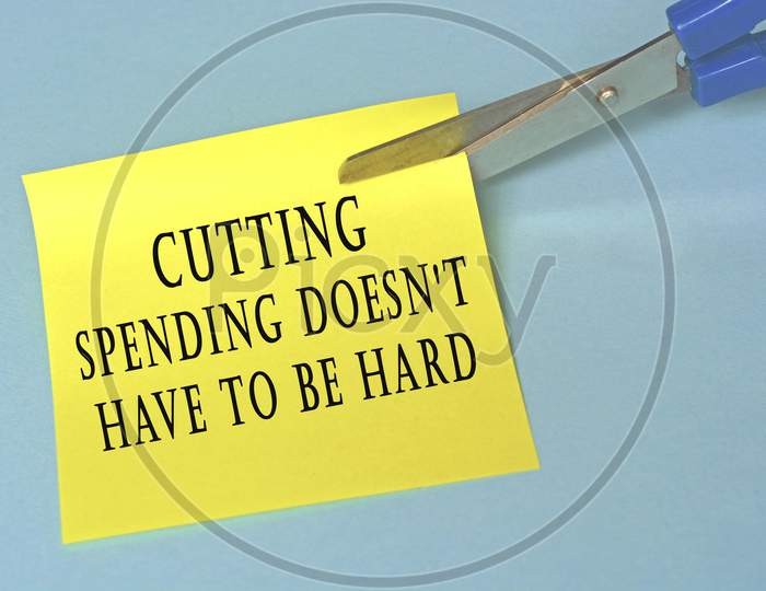 Scissors that cut yellow notepad with text on a blue background. Spending concept