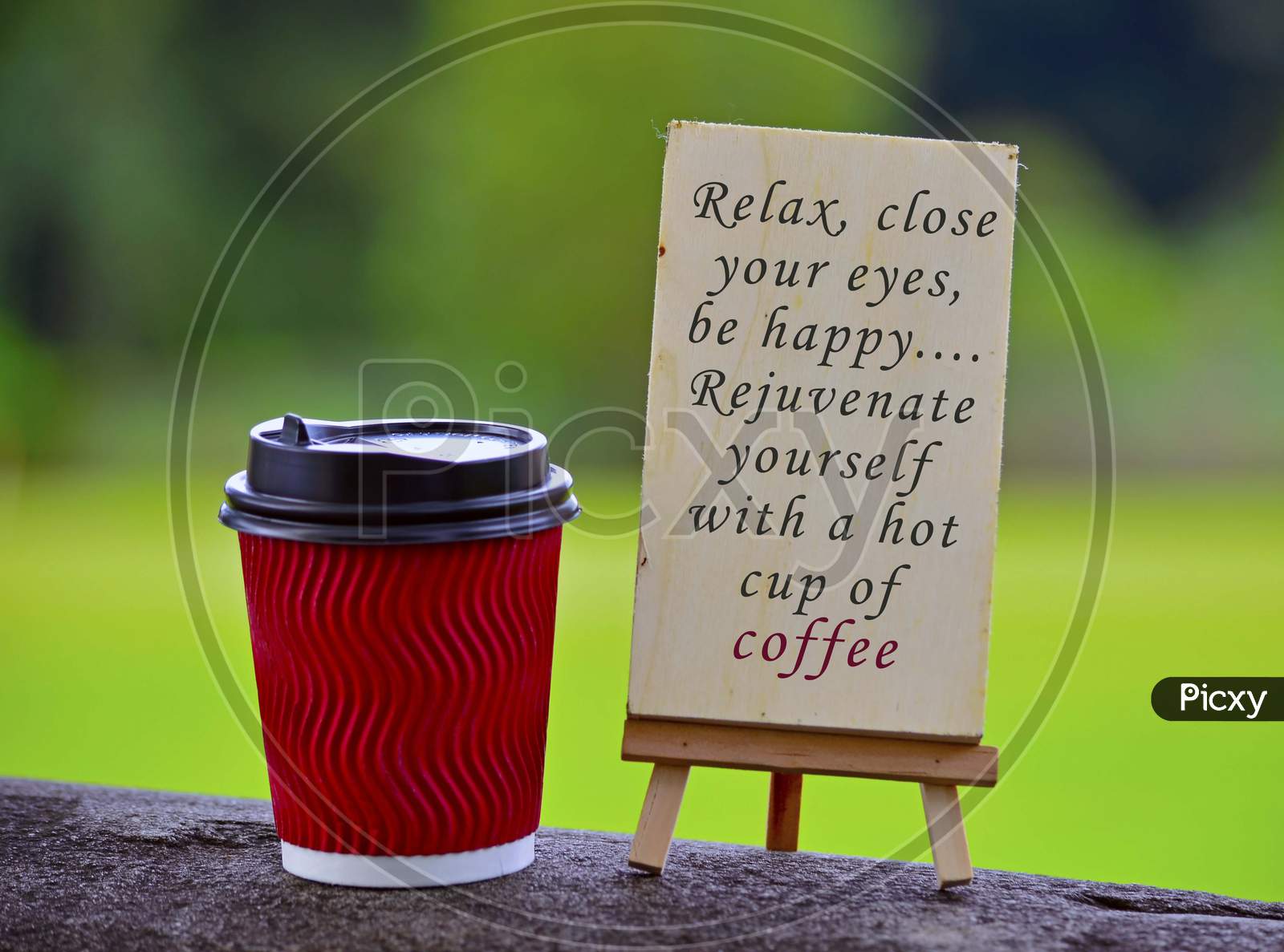 Red paper cup of coffee with text written on chalkboard and greenery background