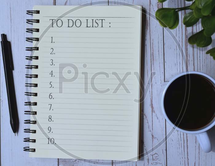 To do list on notepad with cup of coffee, pen and green leaf background on wooden desk. To do list