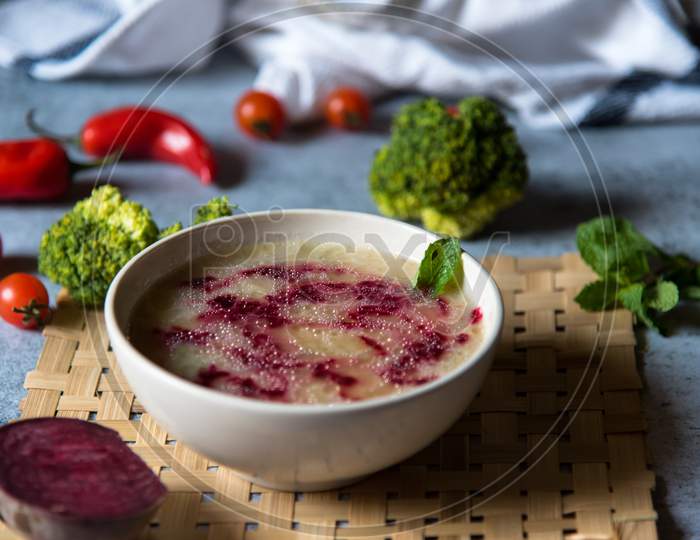 Healthy food chicken and beetroot soup in a bowl along with raw condiments on a background