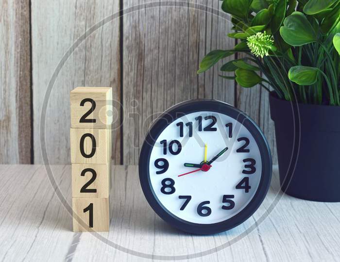 2021 numbers on wooden block cube with alarm clock and potted plant. New year concept