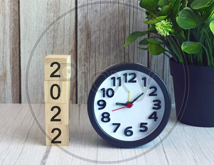 2022 numbers on wooden block cube with alarm clock and potted plant. New year concept