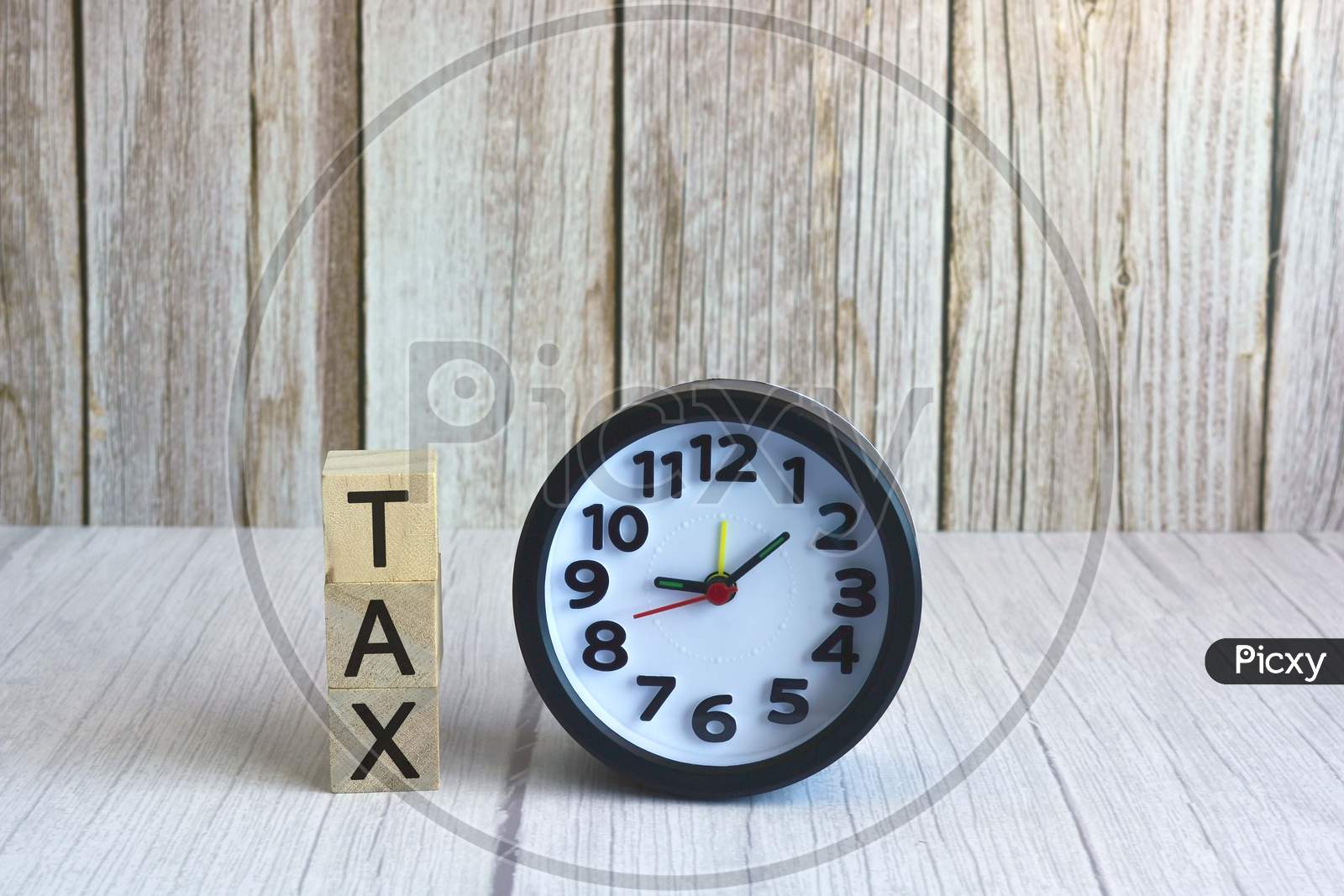 Tax text on wooden block cube with alarm clock. Tax concept
