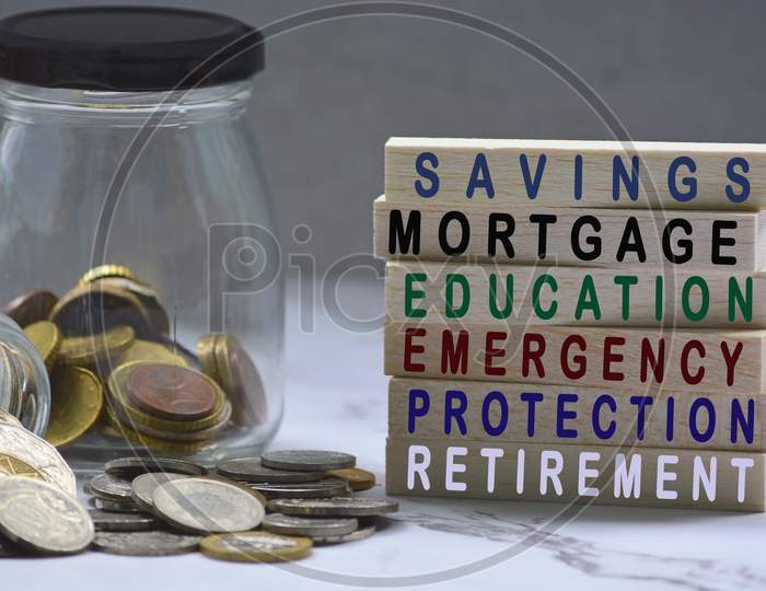 Text on wood block and glass jars with multicurrency coins - Savings, mortgage, educations, emergency, protection, retirement