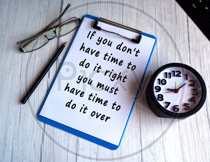 Motivational and inspirational quote on blue clip board with alarm clock, glasses, pen and keyboard on wooden desk - If you do not have time to do it right you must have time to do it over