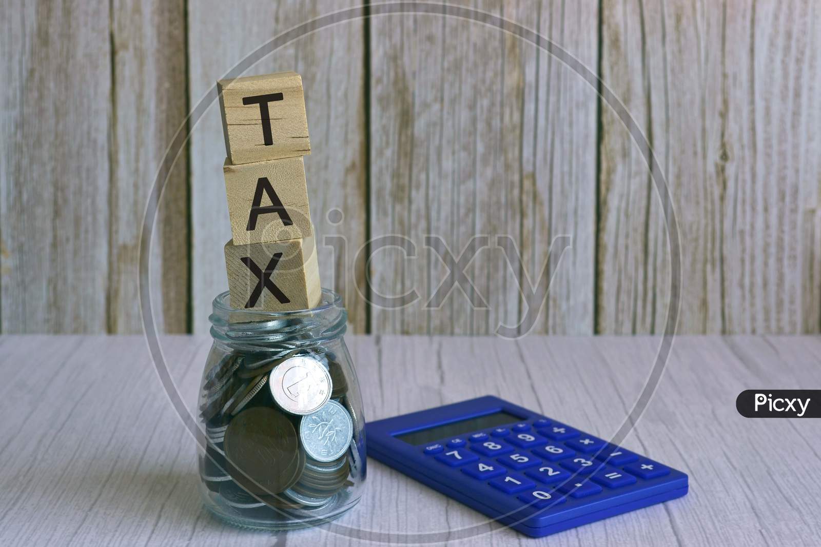 Tax text on wooden block cube on top of glass jar with multicurrency coins and calculator. Tax time concept