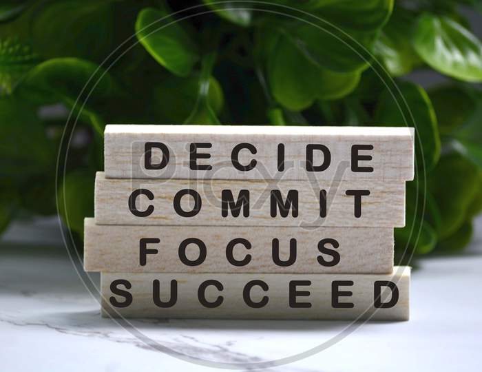 Inspirational words of decide commit focus succeed on wooden blocks with green background
