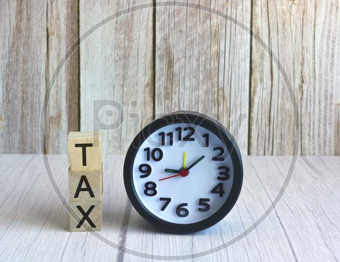 Tax text on wooden block cube with alarm clock. Tax concept