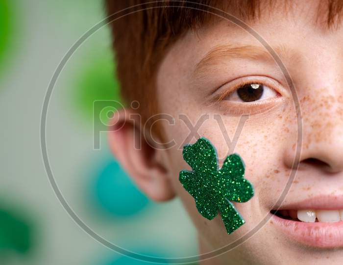 Close Up Of Smiling Kid With Saint Patricks Day Shamrock Leaf On Kids Face During Festival Celebration Wih Copy Space