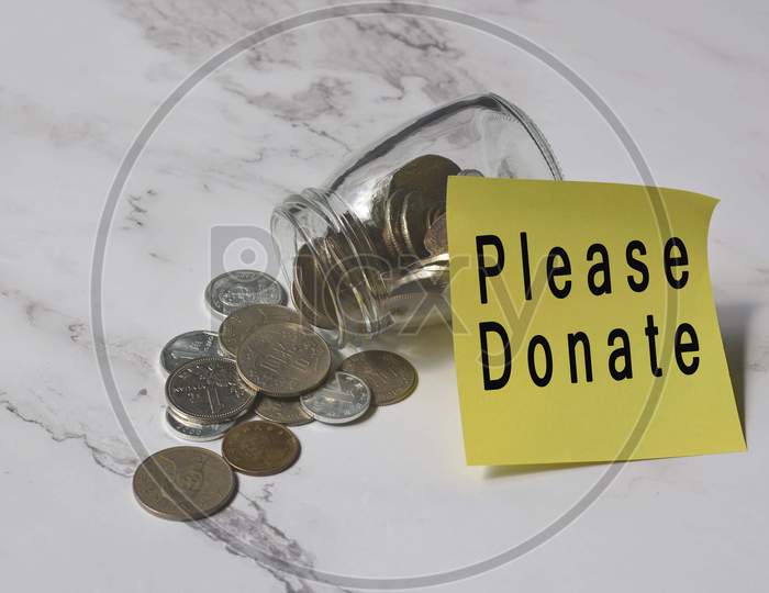Text on yellow notepad stick on a jar with Chinese yuan coins on the white table surface - Please donate