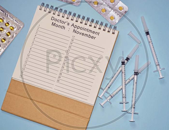 Month of November Doctor's Appointment calendar with disposable injection syringe and medicine on blue background