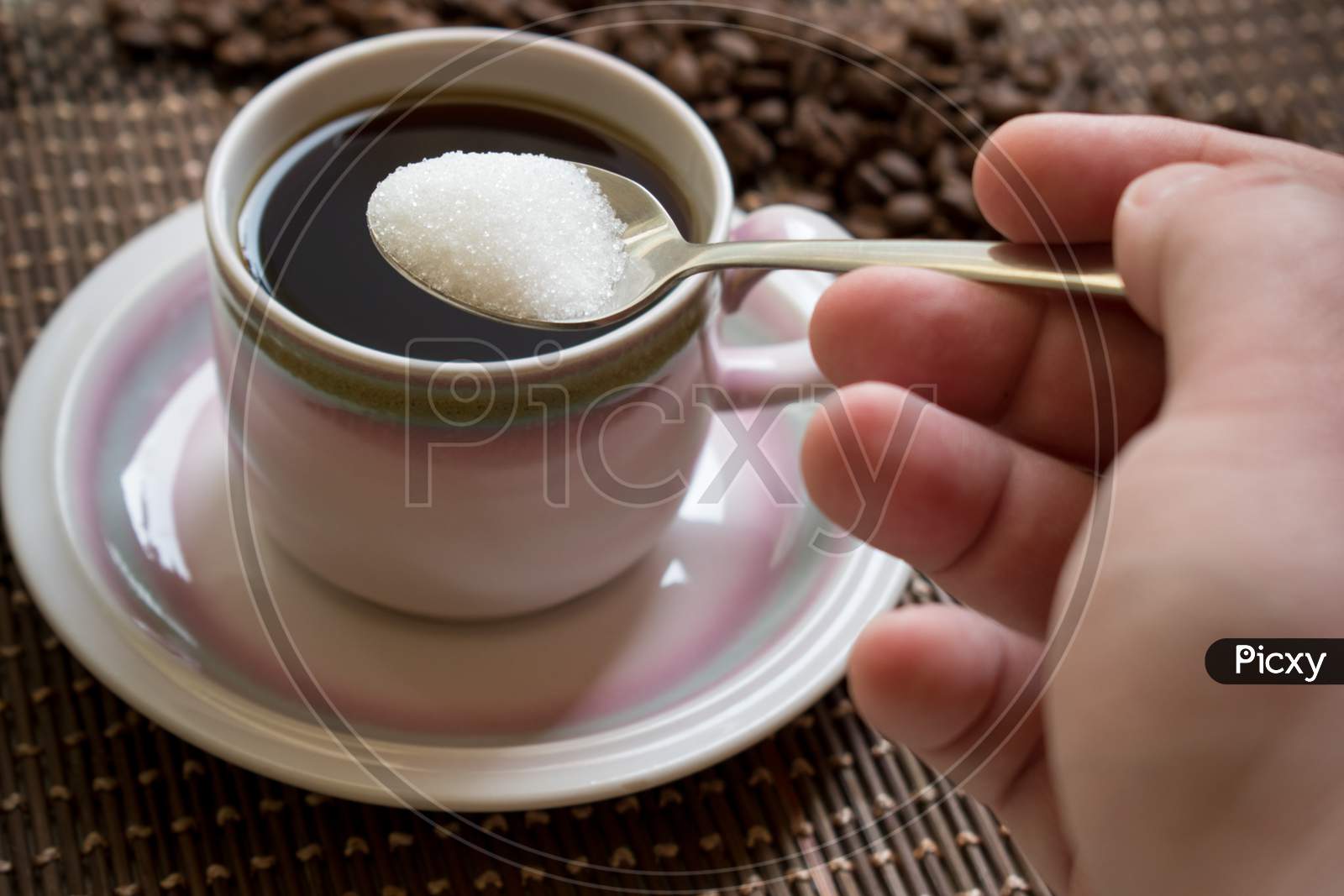 Hand Adding Sugar With Spoon Over A Cup Of Coffee