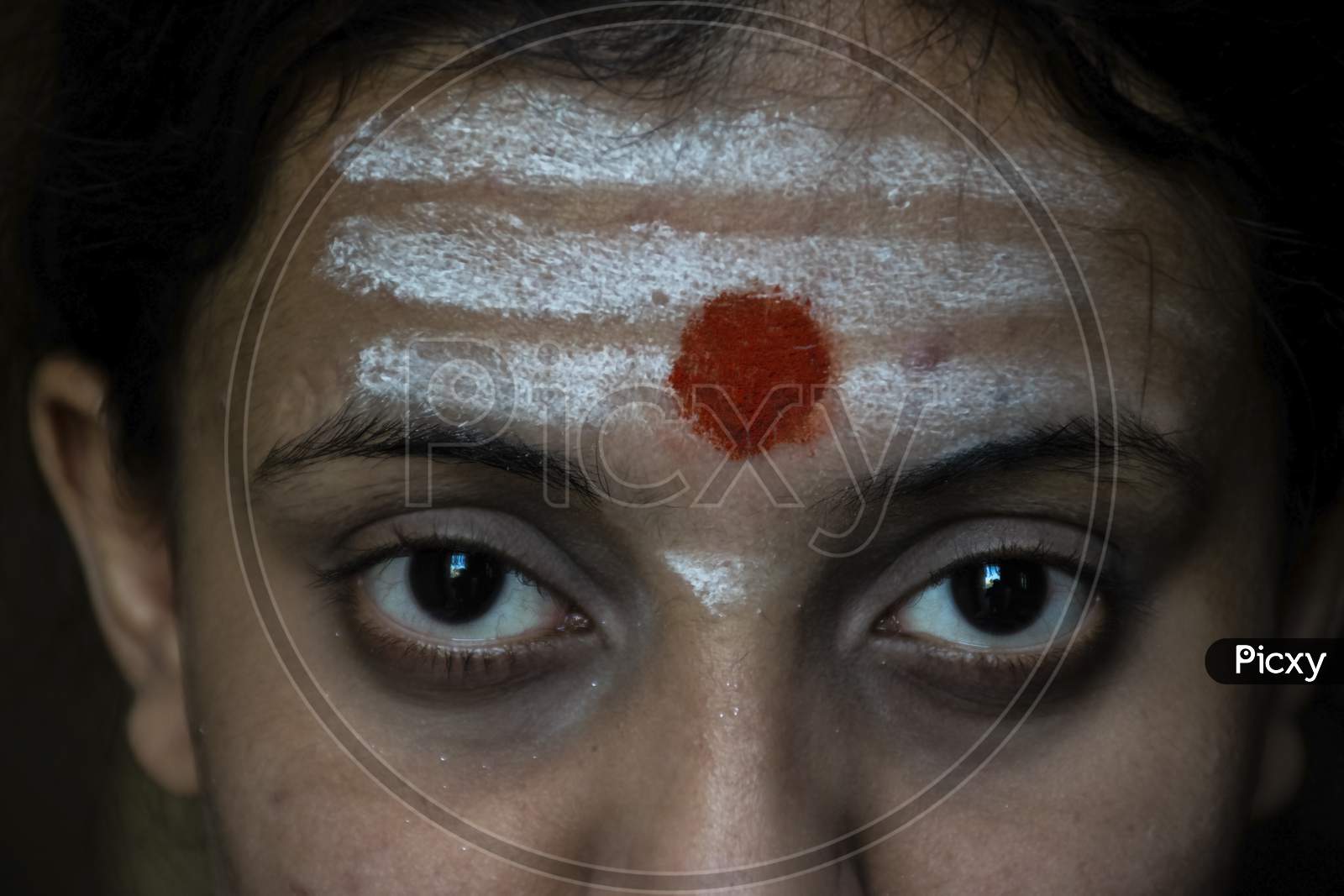 Stock Photo Of A Beautiful 20 To 30 Aged Indian Hindu Girl Who Apply Horizontal White Color Vibhuti And Round Shape Red Color Sindur Tilak Or Vermillion Tilak On Her Forehead Looking At Camera.