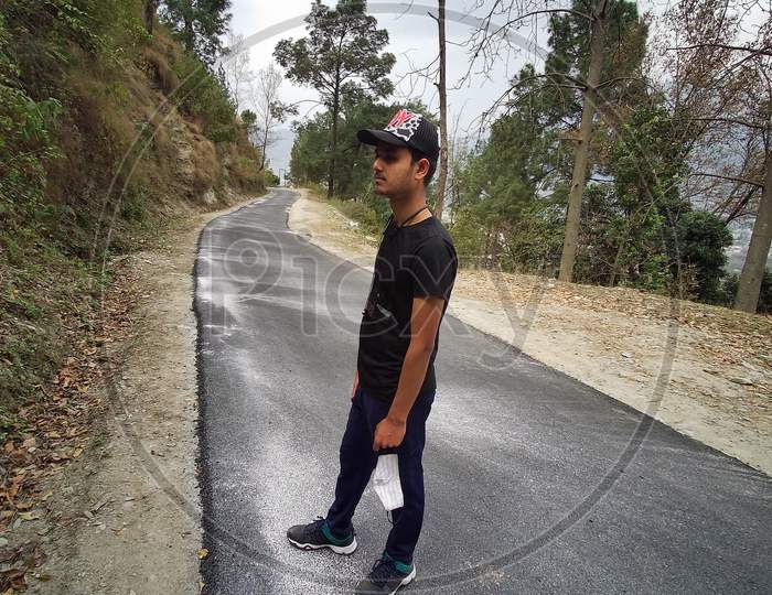 A BOY STANDING AN A ROAD AND MASK ON HIS HAND