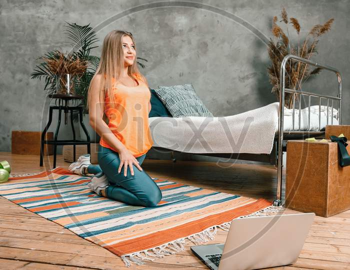A Young Woman Goes In For Sports At Home, Online Workout . The Athlete  Stretching , Meditating, Sitting On A Floor  In The Bedroom