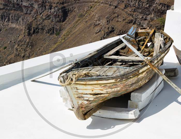 Santorini, Greece: A Wrecked Boat On A Roof At Firostefani Near Fira On A Greek Island Named Santorini. In The Background Is Skaros Rock Mountain Of Imerovigli