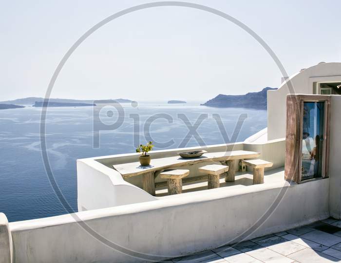 Santorini, Greece - September 11, 2017: A Pot With Flower Or Plant And A Plate On A Wooden Table With Ocean Background