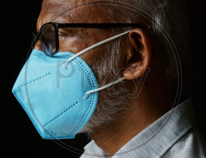 Portrait Of 60 Years Old Indian Man Wearing A Blue Mask, Isolated On A Black Background, In Order To Protect Himself From Covid-19.