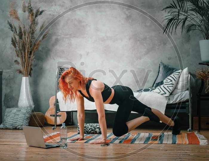 A Cheerful Athlete With Blond  Hair Lunges In The Bedroom With Online Training. The Young Woman Goes In For Sports At Home.