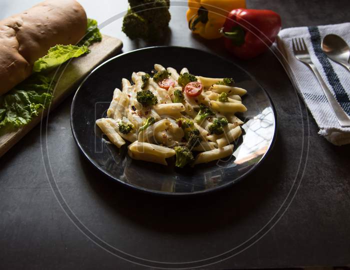Pasta with vegetables and cheese along with bread loaf and condiments
