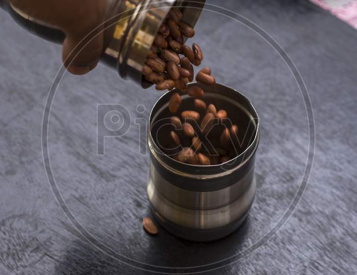 A Female Hand Pouring Kidney Been Or Rajma From One Steel Jar To Another Jar.