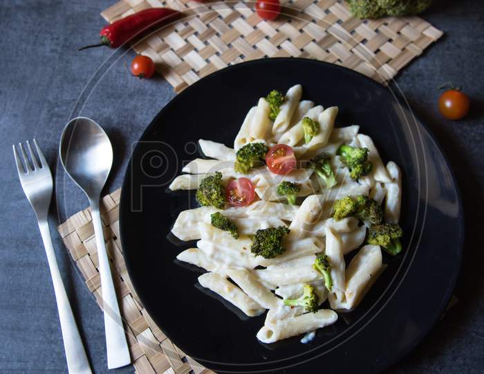 View from top of penne cheese pasta with broccoli in a black plate.