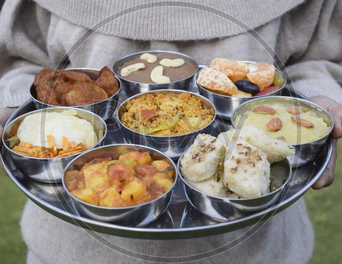 Traditional Farali Indian Food Served In Thali And Bowls With Many Items For Upawaas Upwas Or Vrat Ka Khana. Decorated With Flowers Petals For Fasting Days Food In India. Female Serving Indian Thaali
