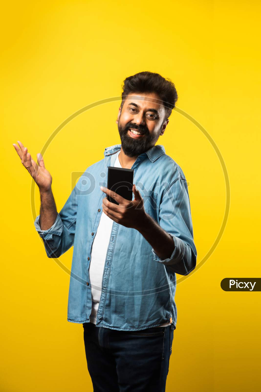 Happy Indian Bearded Young Man Using Smartphone While Standing Against Yellow Background