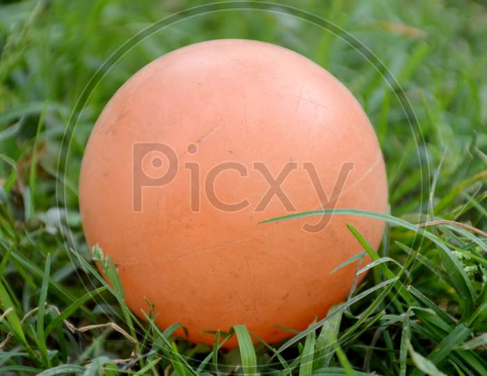 The Orange Color Old Cricket Ball On The Green Grass In The Ground.