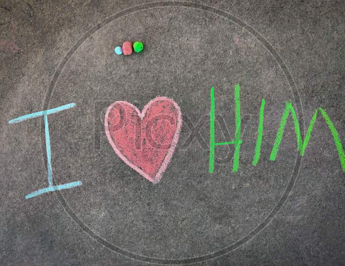 The Inscription Text On The Grey Board, I With Hand Drawn Love Symbol And Him . (I Love Him). Using Color Chalk Pieces.