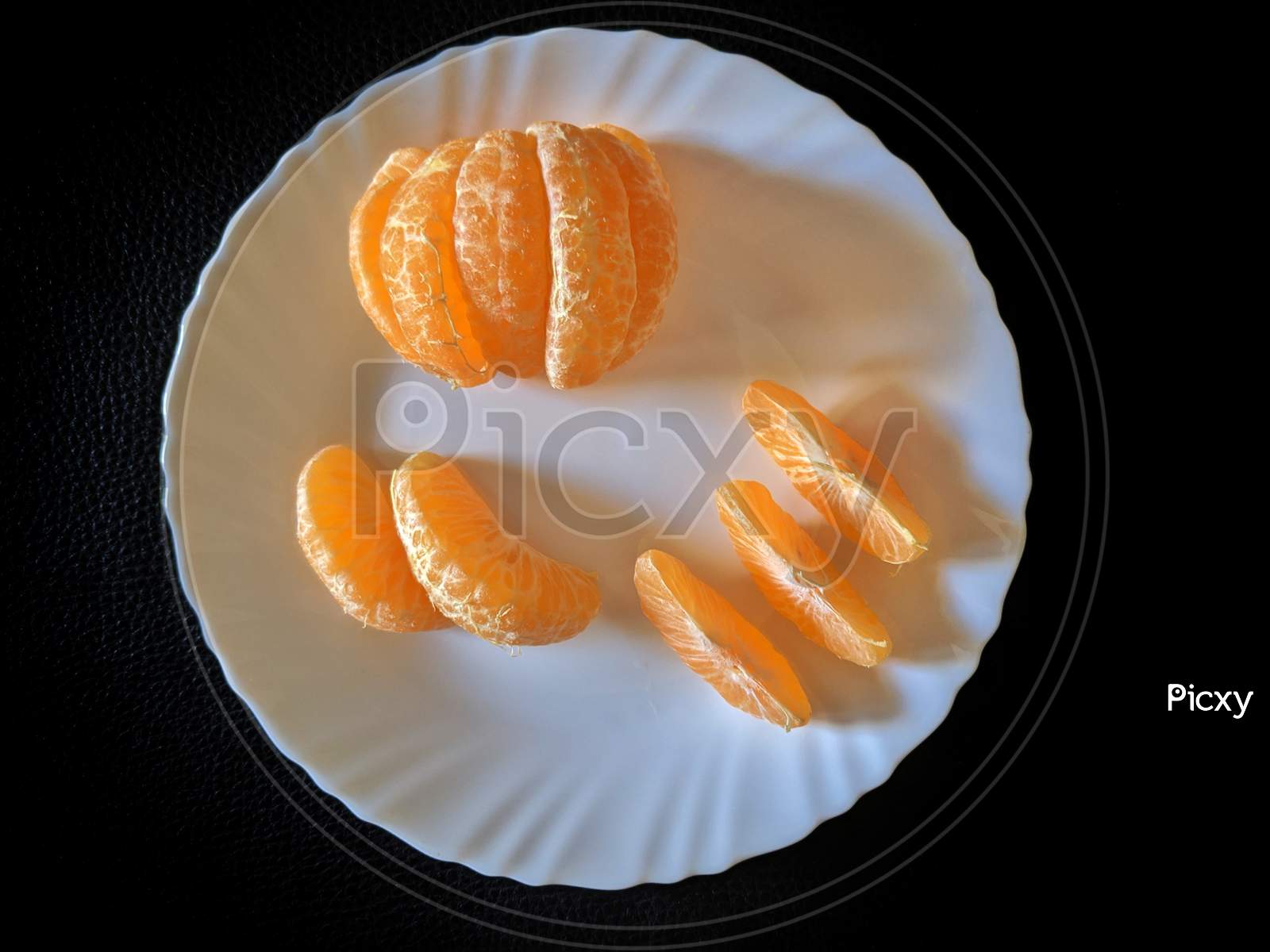 Freshly Cut Natural Healthy Juicy Organic Orange Slices Or Segments On A White Plate, Against A Black Wooden Table, Flat Lay Composition With No People,